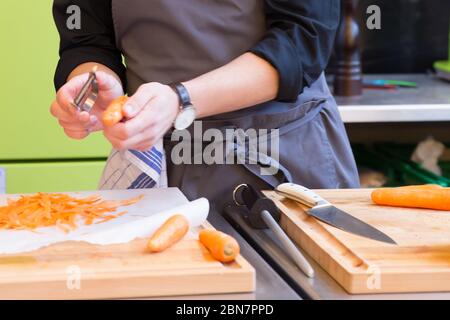 Mann schält Karotten und bereitet eine Mahlzeit auf einem Holzhackbretter Stockfoto