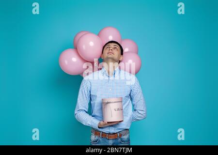 Glücklich kaukasischen Mann hält Geschenkbox und pastellrosa Luftballons auf blauem Hintergrund isoliert. Geburtstagsfeier. Stockfoto