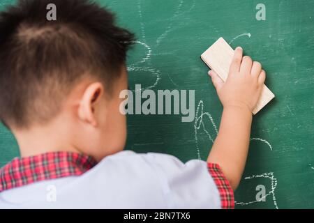 Zurück zur Schule. Zurück von asiatischen niedlichen kleinen Kind junge Kindergarten Vorschule in Schüler Uniform wischen sauber oder löschen Kreide auf grünen Schule Tafel w Stockfoto