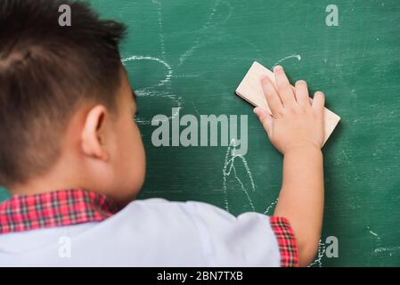 Zurück zur Schule. Zurück von asiatischen niedlichen kleinen Kind junge Kindergarten Vorschule in Schüler Uniform wischen sauber oder löschen Kreide auf grünen Schule Tafel w Stockfoto