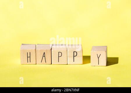 Holzwürfel mit dem Wort Happy auf hellem gelbem Hintergrund, fröhliches Konzept Stockfoto