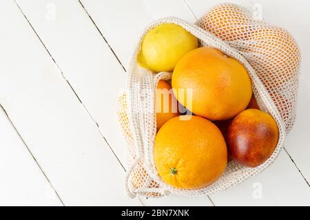Orange, Zitrone und Grapefruit in Öko-Tasche auf weißem Holzhintergrund. Zitrusfrüchte. Zero Waste, umweltfreundliches oder plastikfreies Lifestyle-Konzept. Kopierbereich, vertikal. Stockfoto
