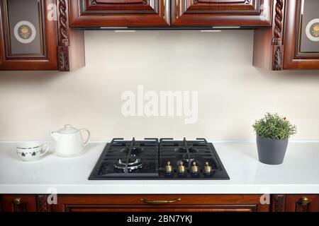 Interieur der modernen Küche im klassischen Stil mit goldenen Elementen Kirschbaum Erle Holzschränke mit eingebauten Geräten, Gasherd und Dunstabzugshaube mit Stockfoto