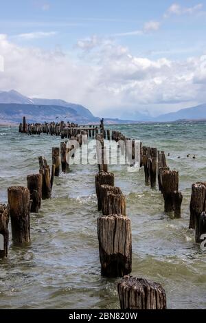 Holzpfosten von einem alten Pier, Puerto Natales, Patagonien, Chile, Cerro Monumento Moore im Hintergrund. Stockfoto