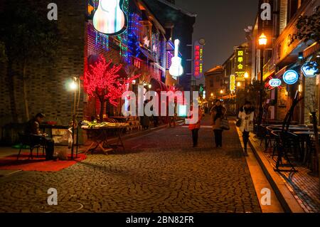 Drei Damen Fuß entlang einer gepflasterten Fußgängerzone. Ein Mann wartet auf Kunden an seinem Grill Stand in Laowaitan, Ningbo Stockfoto