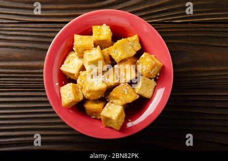 Flach legen Nahaufnahme Blick auf knusprig tief rühren gebratenen Tofu Würfel mit Schnittlauch in Tonschale auf hölzernen Küchentisch Stockfoto