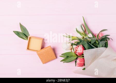 Flache Lage Zusammensetzung kleine offene leere Geschenkbox neben Bouquet von frischen Blumen auf rosa Holzhintergrund. Stockfoto