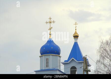 Orthodoxe christliche Kirche mit weißen Wänden, blauen Kuppeln und goldenen Kreuzen in Russland. Ein Gebäude für religiöse Zeremonien mit einem Glockenturm vor einem bewölkten Himmel auf dem Land. Stockfoto