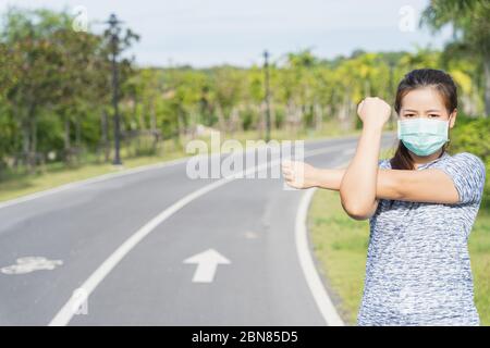 Junge Frau, die medizinische Maske trägt und die Arme vor dem Training im Park dehnt. Bleiben Sie in fit während der Quarantäne in den Tagen der th Stockfoto