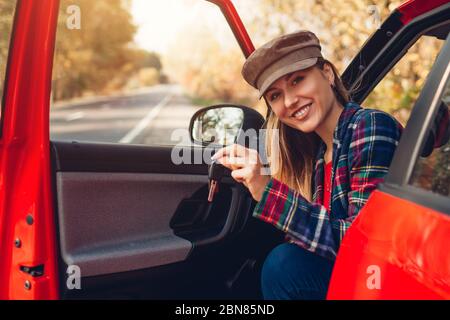 Junge Frau hält Schlüssel des neuen Autos. Glücklicher Fahrer, der auf Kamera schaut, die im Auto sitzt. Glücklicher Käufer kaufte rote autimobile. Stockfoto