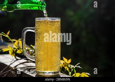 Bier in Glas aus der Flasche auf der Sommerterrasse gießen. Stockfoto