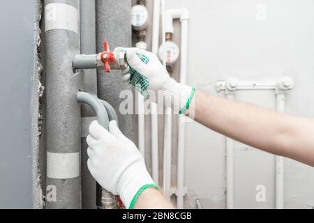 Männlicher Klempner prüft Rohre für zentrale heiß- und Kaltwasserversorgung der Wohnung Stockfoto