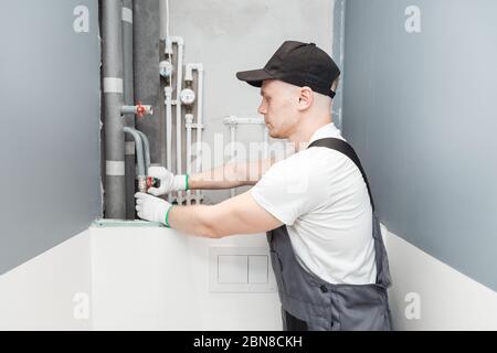 Männlicher Klempner prüft Rohre für zentrale heiß- und Kaltwasserversorgung der Wohnung Stockfoto