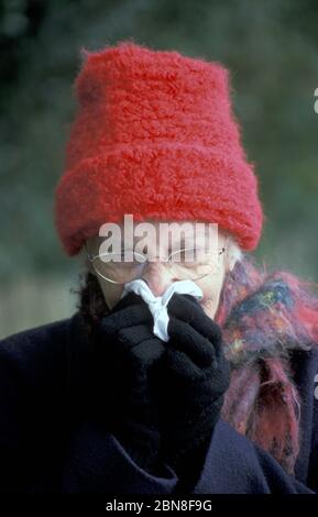 Ältere Frau in Winterkleidung weht Nase Stockfoto