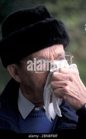 Älterer Mann in Winterkleidung weht Nase Stockfoto