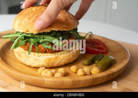 Veganer Falafel Hummus Burger mit hausgemachtem Sauerteig-Brötchen, Tomaten, eingelegten Gurken und Rucola in einem Holzteller Stockfoto