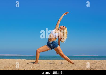 Junge blonde kaukasische Frau Yoga am Strand in der Nähe von Meer zu trainieren Stockfoto