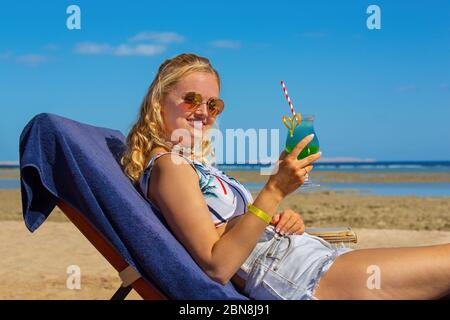 Junge kaukasische Frau trinkt alkoholischen Cocktail auf Strandbett Stockfoto