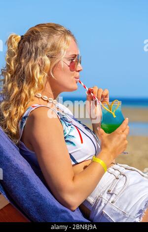 Junge kaukasische Frau trinkt Cocktail am Strand in der Nähe des Meeres Stockfoto