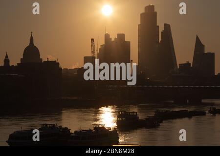 Sunrise in London schafft eine Silhouette der City of London und der St Paul's Cathedral mit der Themse und vertäuten Vergnügungsbooten im Vordergrund. Stockfoto