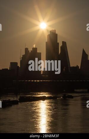 Sunrise in London schafft eine Silhouette der City of London mit der Themse und den Flussbooten im Vordergrund. Stockfoto