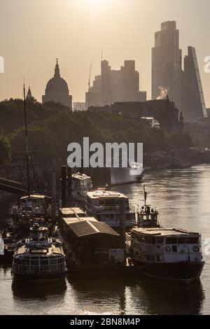 Sunrise in London schafft eine Silhouette der City of London und der St Paul's Cathedral mit der Themse und vertäuten Vergnügungsbooten im Vordergrund. Stockfoto