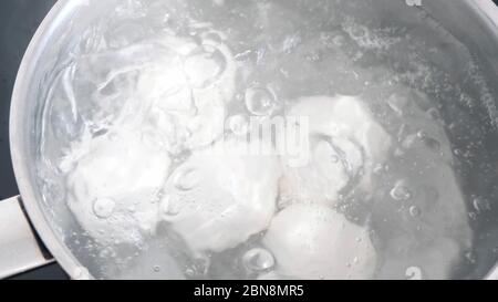Hühnereier, die in einer Edelstahlpfanne in Wasser kochen. Stockfoto