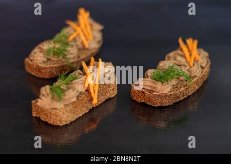 Frisch hausgemachte Hühnerleber Pastete mit Karotten, Zwiebeln und Butter. Garniert mit einem Zweig Dill. Auf Brot geschmiert. Auf schwarzem Hintergrund. Kopie sp Stockfoto