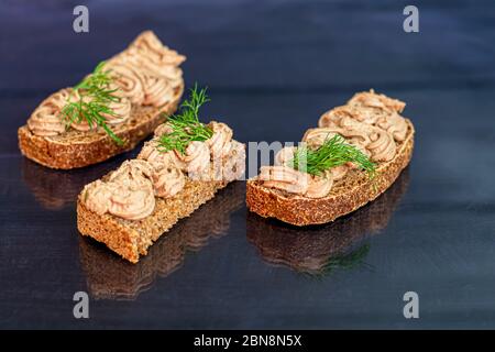 Frisch hausgemachte Hühnerleber Pastete mit Karotten, Zwiebeln und Butter. Garniert mit einem Zweig Dill. Auf Brot geschmiert. Auf schwarzem Hintergrund. Kopie sp Stockfoto