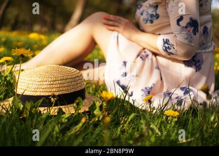 Frau mit einem Strohhut in einem Blumenfeld und grünem Gras. Sommer auf dem Land. Konzentrieren Sie sich auf Hut Stockfoto