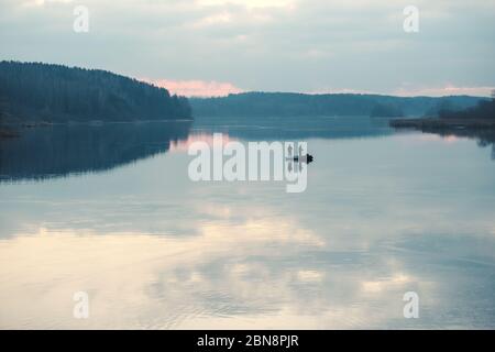 Silhouetten von Fischern in einem Boot auf einer Seeoberfläche. Stockfoto