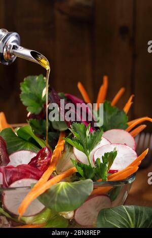 Gemüsesalat mit Olivenöl Dressing auf rustikalem Hintergrund. Olivenöl Stream und gesunde frische Gemüsesalat. Olivenöl in eine Schüssel mit Grün gießen Stockfoto
