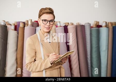 Porträt der Designerin in Brillen lächelnd in die Kamera, während Notizen in Notizblock und Planung ihrer Arbeit in der Werkstatt Stockfoto