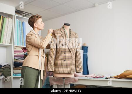 Junge Schneider Messungen von Jacke auf Schaufensterpuppe während der Arbeit in der Werkstatt Stockfoto