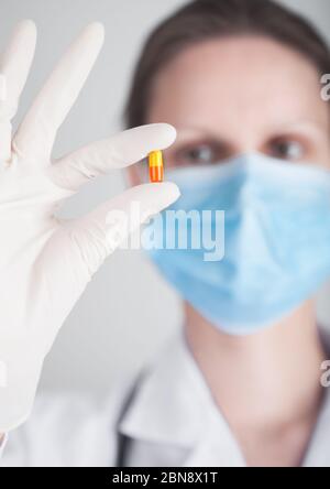 Arzt trägt blaue Gesicht medizinische Maske und klare Latexhandschuhe mit Tablette Pille auf grauen Krankenhaus Wand Hintergrund. Registerkarte Antibiotika und Virusbehandlung Stockfoto