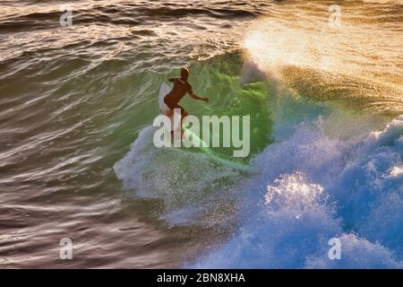 Unerkennbarer Surfer, der eine letzte Welle des Tages auf Maui reitet. Stockfoto