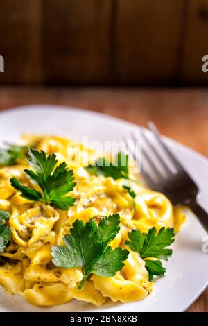 Ravioli mit frischen Petersilienblättern auf rustikaler Holzfläche. Traditionelle italienische Küche. Gekochte Ravioli-Pasta in Gericht unter cremiger Sauce auf CO Stockfoto