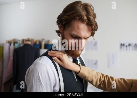 Bärtiger junger Mann besucht seinen Designer und versucht, den Anzug in der Werkstatt Stockfoto