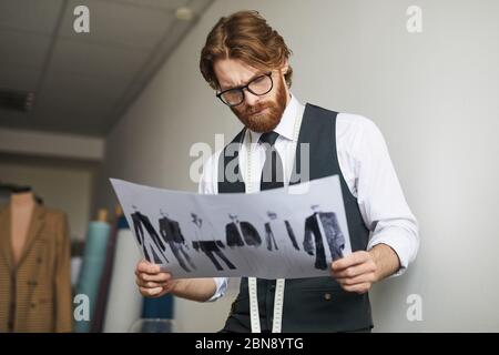 Seriöse Modedesignerin in Brillen, die mit Skizzen der neuen Kleider-Kollektion arbeitet Stockfoto