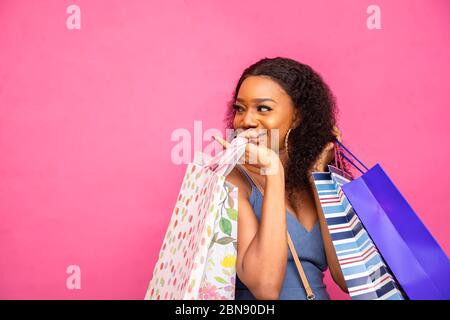 Schöne afrikanische Dame trägt Einkaufstaschen, lächelnd, und Gefühl aufgeregt auf rosa Hintergrund, suchen und zeigen auf die , Nahaufnahme Stockfoto