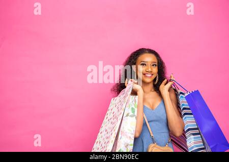 Hübsche schwarze Dame, die Einkaufstaschen hält und lächelt, auf rosa Hintergrund Stockfoto