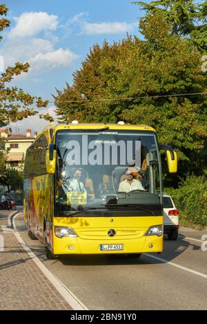 GARDA, ITALIEN - SEPTEMBER 2018: Gelber Reisebus, der auf einer Straße in der Stadt Garda am Gardasee fährt. Stockfoto