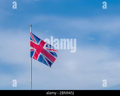 Flagge der britischen Union Jack fliegt auf einem Fahnenmast in einer Brise mit blauem Himmel und Kopieraum. Stockfoto