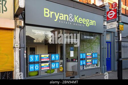 London, Vereinigtes Königreich - 04. April 2020: BLEIB ZUHAUSE & SICHERE Schilder an den Fenstern der Immobilienagentur Bryan & Keegan. Die meisten nicht unbedingt notwendigen Geschäfte sind d geschlossen Stockfoto