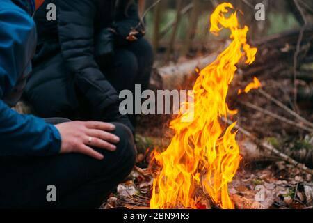 Der Mensch wärmt seine Hände auf Feuer. Brennendes Holz am Abend im Wald. Lagerfeuer im touristischen Camp in der Natur. Grillen und Kochen im Freien frische Luft Stockfoto