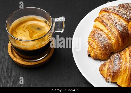 Tasse Kaffee und frisch gebackene Croissants auf einem dunklen Tisch. Frühstück Konzept serviert. Französischer Teig aus Blätterteig Stockfoto