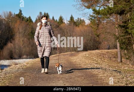 Junge Frau in warmer Jacke, trägt Virus Gesicht Mundmaske, geht ihren Hund auf Landstraße. Masken sind bei Coronavirus-Covid- Stockfoto