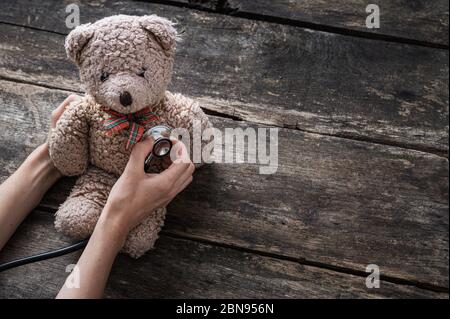 Die Hand der Kinderärztin, die Stethoskop verwendet, um einem Teddy zuzuhören, trägt Herz oder Lunge in einem konzeptionellen Bild der pädiatrischen Gesundheitsversorgung. Stockfoto