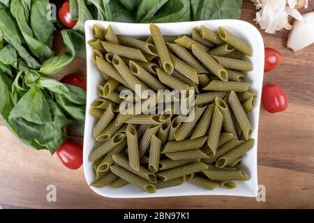 Glutenfreie Penne Pasta aus grünen Erbsen auf Holzbrett. basilikum, Tomaten und Knoblauch. Schuss von oben und closeup.Food Hintergrund italienische Penne Stockfoto