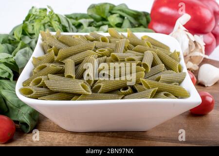 Glutenfreie Penne Pasta aus grünen Erbsen auf Holzbrett. basilikum, Tomaten und Knoblauch. Schuss von oben und closeup.Food Hintergrund italienische Penne Stockfoto